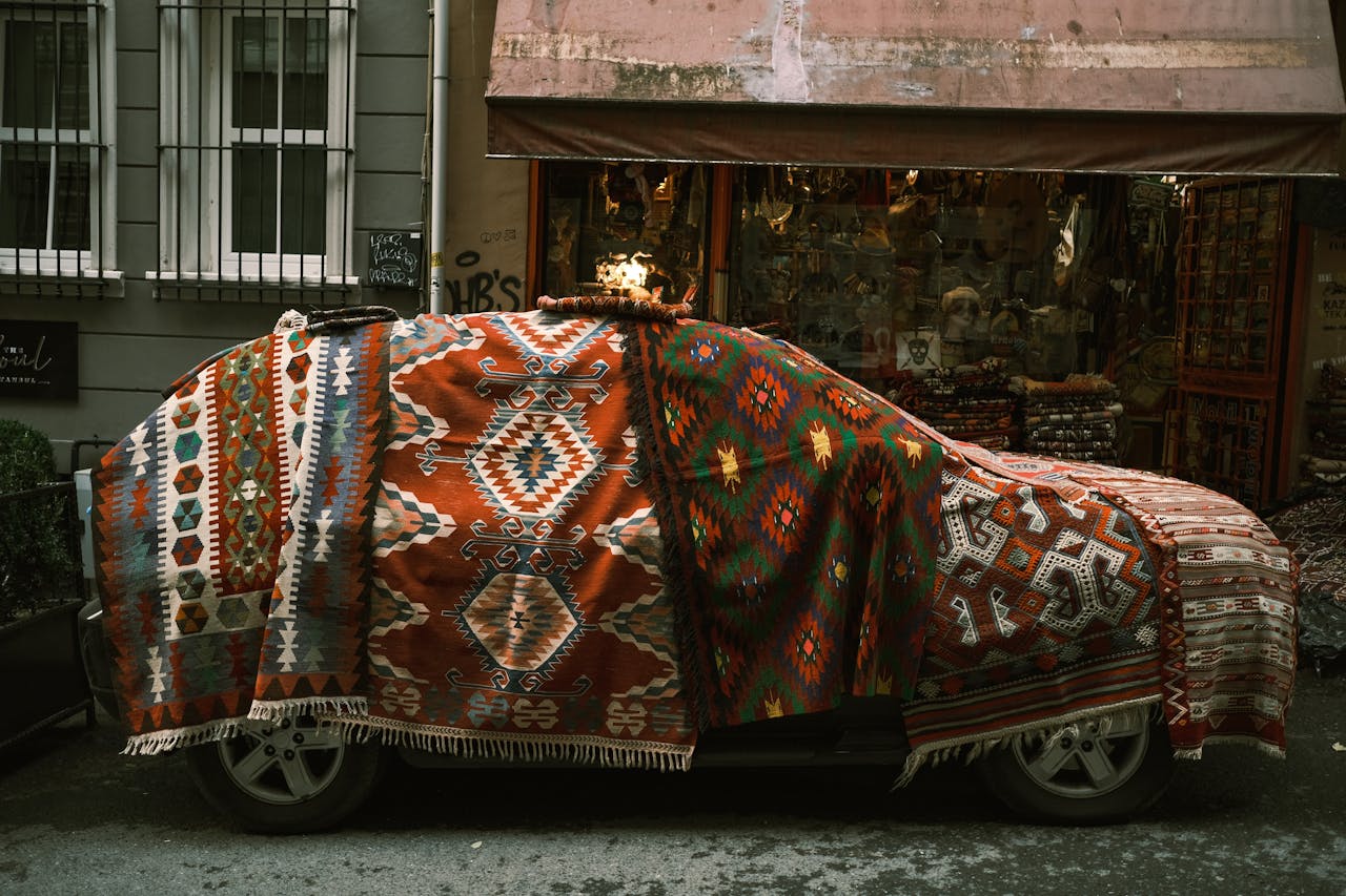 A parked car draped with colorful ethnic blankets outside a textile shop.