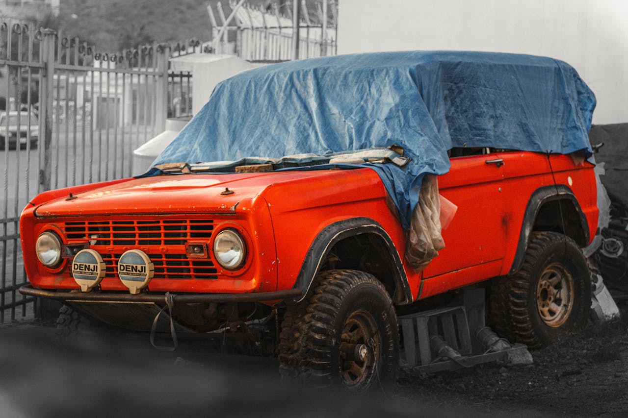 A classic red SUV covered with a blue tarp, parked outdoors, showcasing vintage charm.