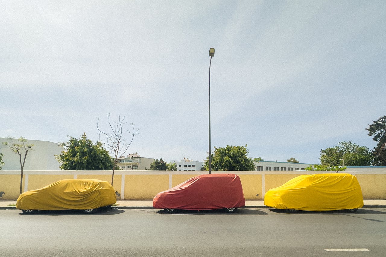 about-us Three covered cars in yellow and red lined up on an urban street under a clear sky.