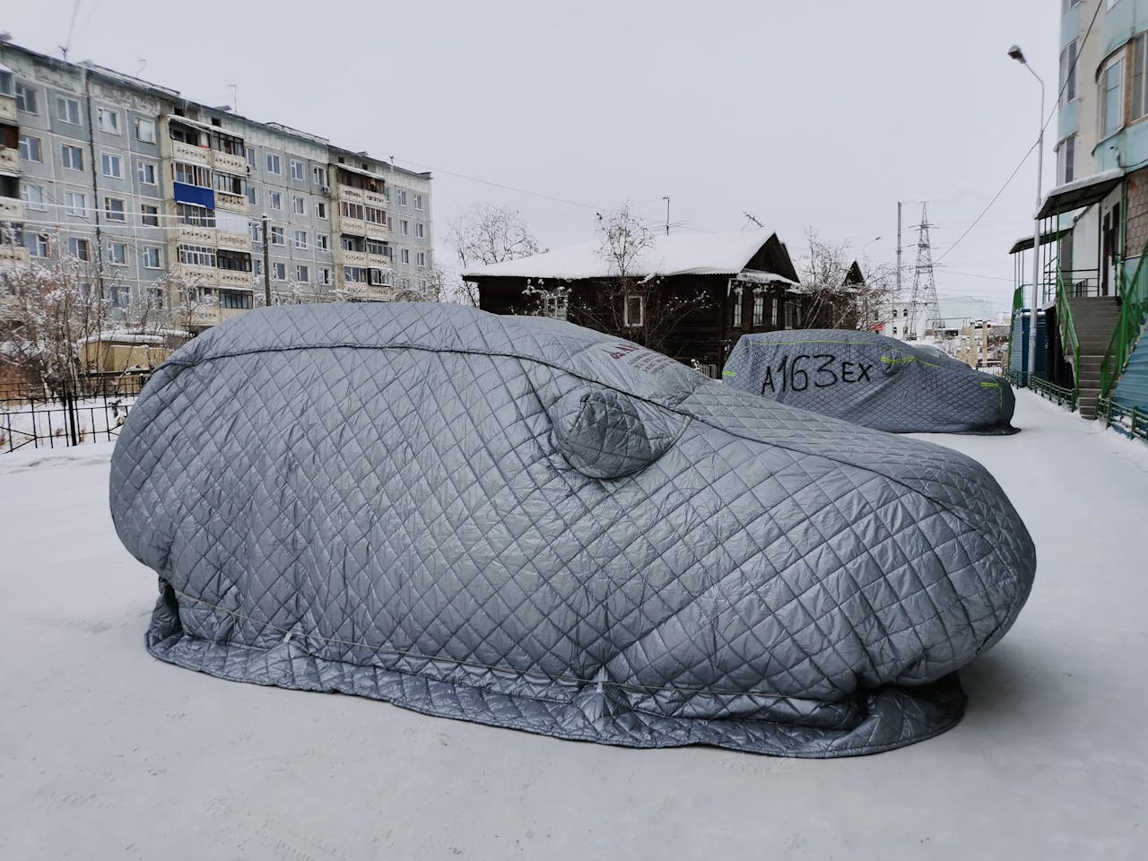 Quilted car covers on snow in a city during winter.